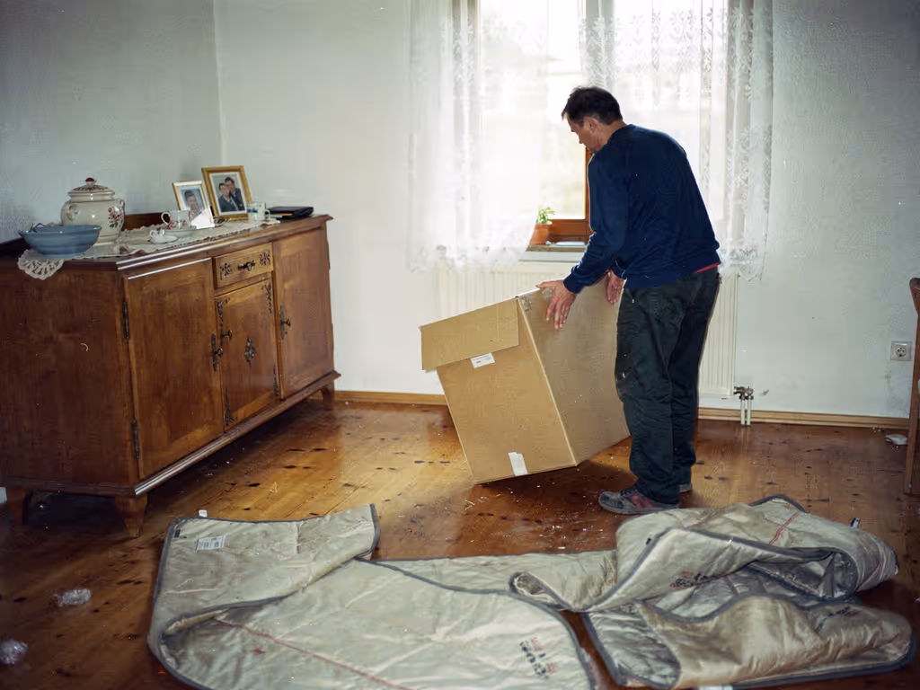 Mitarbeiter räumt bei einer Wohnungsauflösung in Ulm einen Karton aus einem halb leergeräumten Wohnzimmer